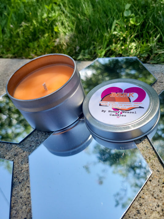 A Dirk Strider Inspired Candle. A silver 4 oz tin with a bright orange beeswax candle inside sits on hexagonal shaped mirrors. The lid sits next to it, baring the hat symbol, the heart aspect symbol, and the title of the candle with a brief description of its scent.